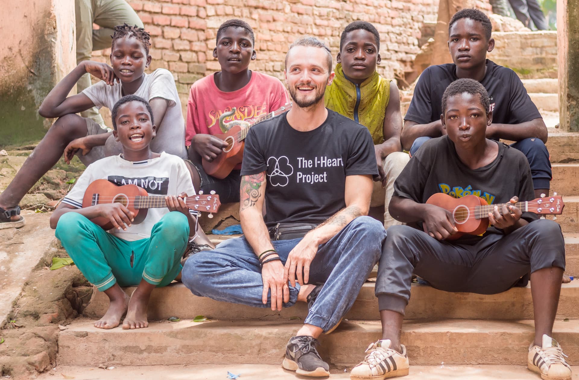 Young people with ukuleles sitting on steps beside a team member