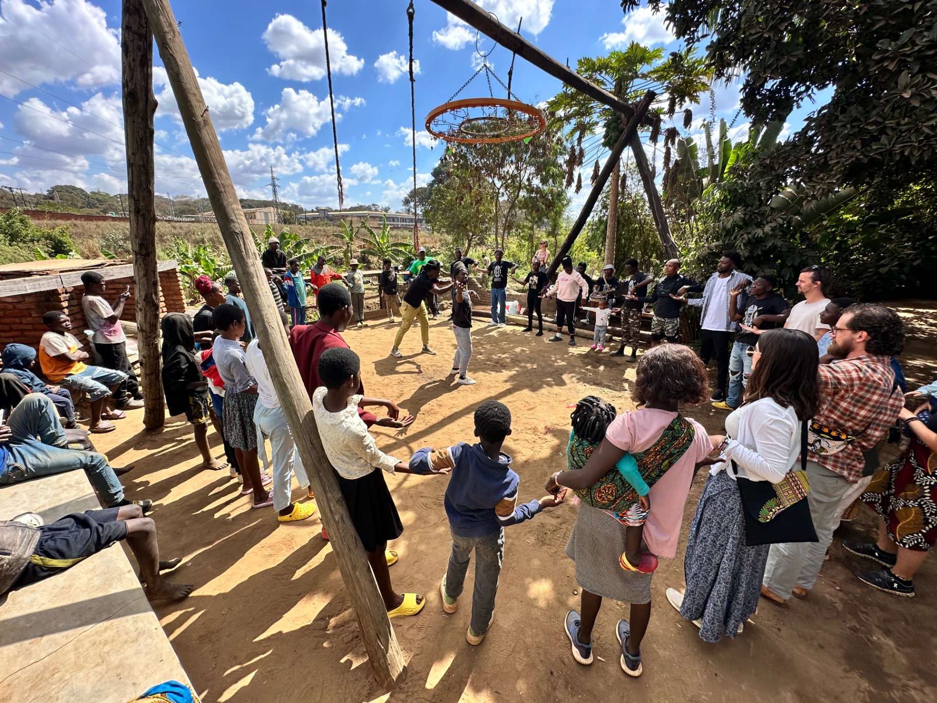 Children and adults holding hands in a large circle game outdoors on a sunny day